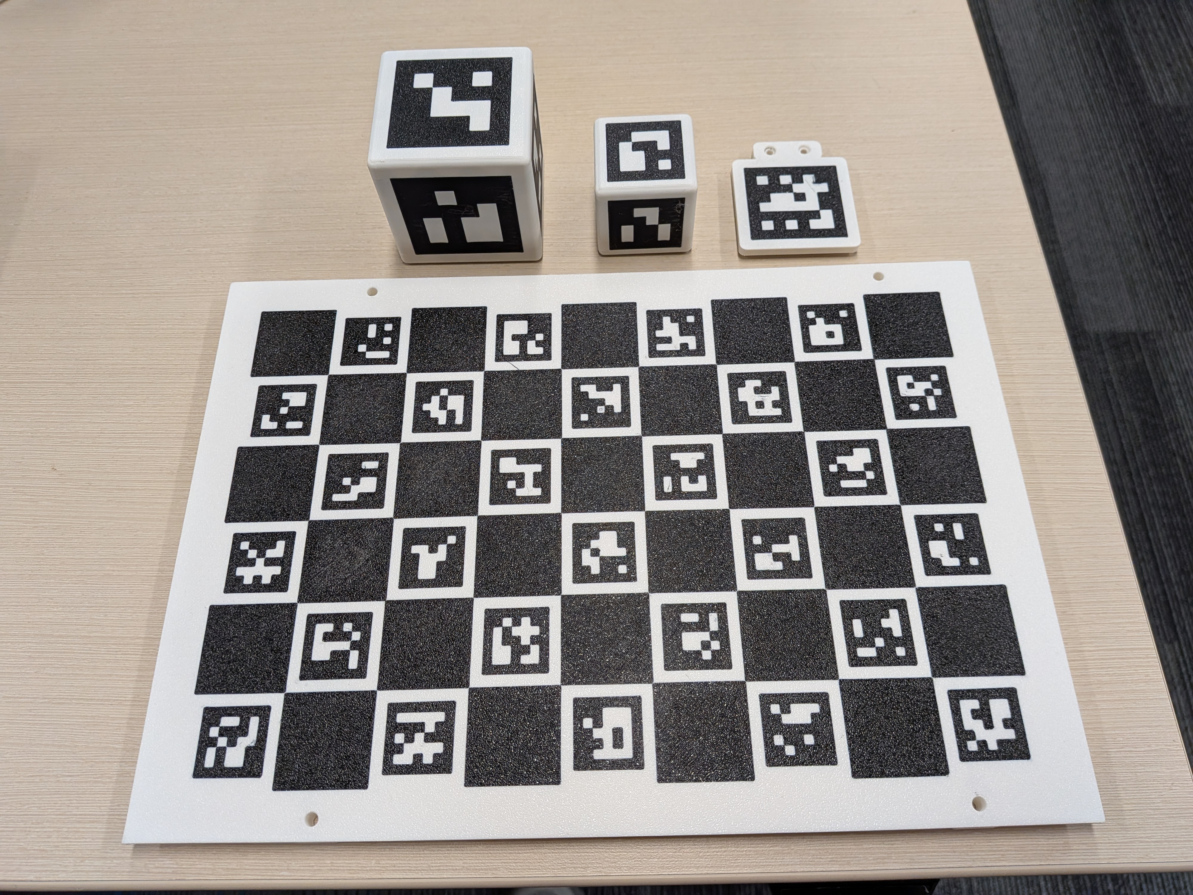 Large and small printed marker cubes, a separate wrist-marker plate with a mounting tab, and a ChArUco board laid out on a table.